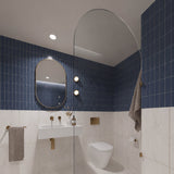 Square navy and white marble-look tiled bathroom with arched glass shower screen, white wall-hung basin and pill-shaped mirror