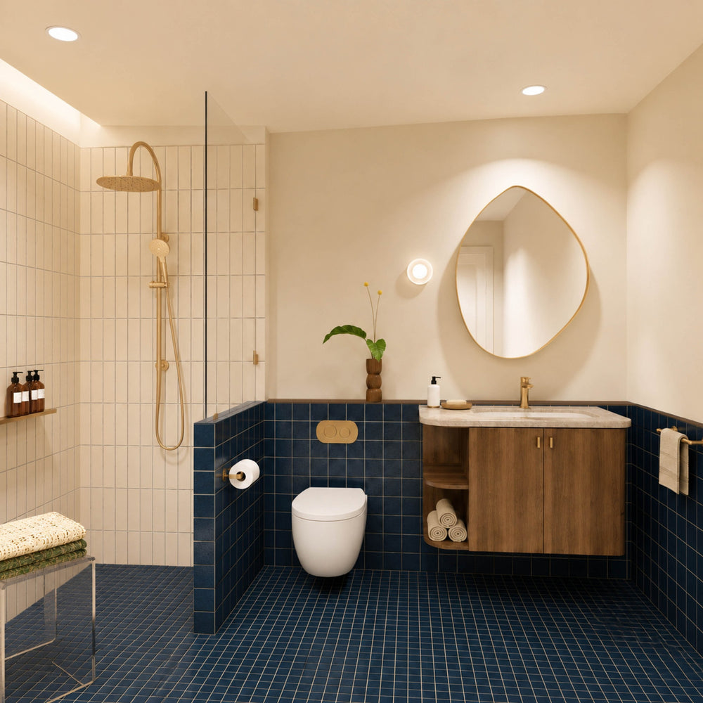 Navy tiled bathroom with walk-in shower, timber vanity, cream stone benchtop, pebble-shaped mirror and gold fittings