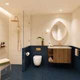 Navy tiled bathroom with walk-in shower, timber vanity, cream stone benchtop, pebble-shaped mirror and gold fittings