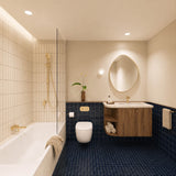 Navy tiled bathroom with shower over bath, timber vanity, cream stone benchtop, pebble-shaped mirror and gold fittings