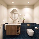 Square navy tiled bathroom with timber vanity, cream stone benchtop, pebble-shaped mirror and wall-hung toilet