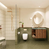 Olive green tiled bathroom with walk-in shower, timber vanity, green stone benchtop, pebble-shaped mirror and gold fittings