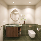 Square olive green tiled bathroom with timber vanity, green stone benchtop, pebble-shaped mirror and wall-hung toilet