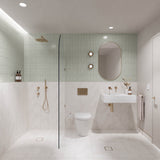 Sage green and white marble-look tiled bathroom with walk-in shower, white wall-hung basin, pill-shaped mirror and gold fittings