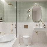 Sage green and white marble-look tiled bathroom with shower over bath, white wall-hung basin, pill-shaped mirror and gold fittings