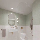 Square sage green and white marble-look tiled bathroom with arched glass shower screen, white wall-hung basin and pill-shaped mirror