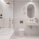 White tiled bathroom with marble-look tiles, shower over bath, white wall-hung basin, pill-shaped mirror and gold fittings