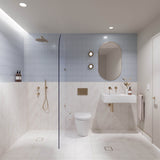 Light blue and white marble-look tiled bathroom with walk-in shower, white wall-hung basin, pill-shaped mirror and gold fittings