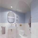 Square light blue and white marble-look tiled bathroom with arched glass shower screen, white wall-hung basin and pill-shaped mirror