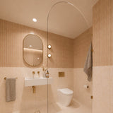 Square peach and cream marble-look tiled bathroom with arched glass shower screen, white wall-hung basin and pill-shaped mirror